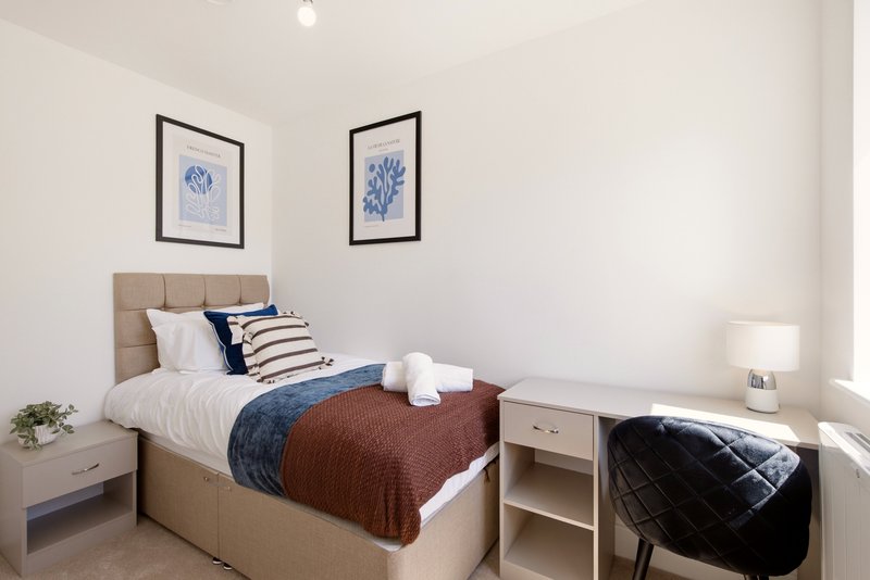 Bedroom with single bed, beige headboard, blue artwork, white bedside table and lamp