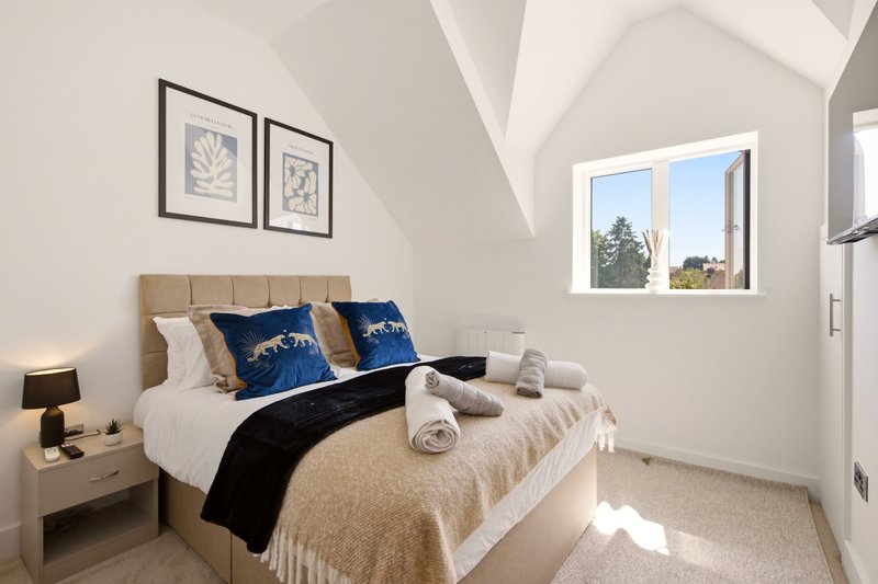 Bright modern bedroom with double bed, blue pillows, rolled towels, and window views