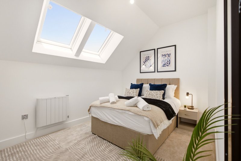 Bright attic bedroom with double bed, skylight windows, neutral bedding and potted plant