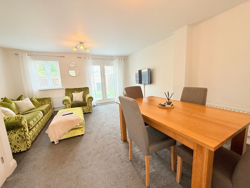 Open-plan living and dining area with green sofas, wooden dining table, and patio doors