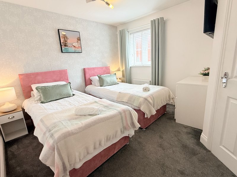 Twin bedroom with pink headboards, white bedding, green cushions, and neutral decor