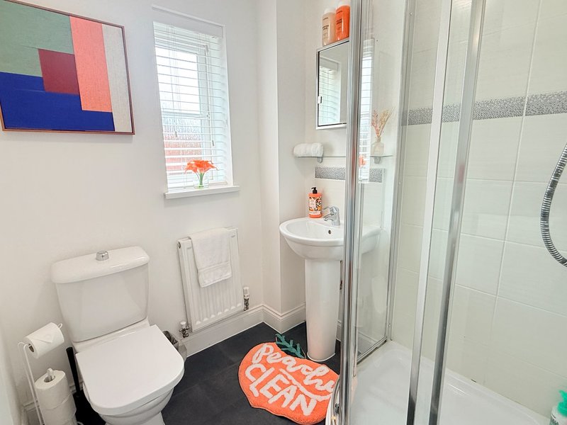 Modern bathroom with toilet, pedestal sink, shower cubicle, and colorful wall art