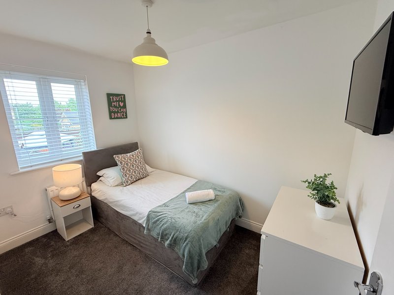 Bright bedroom with single bed, pendant lamp, bedside table, and wall-mounted TV