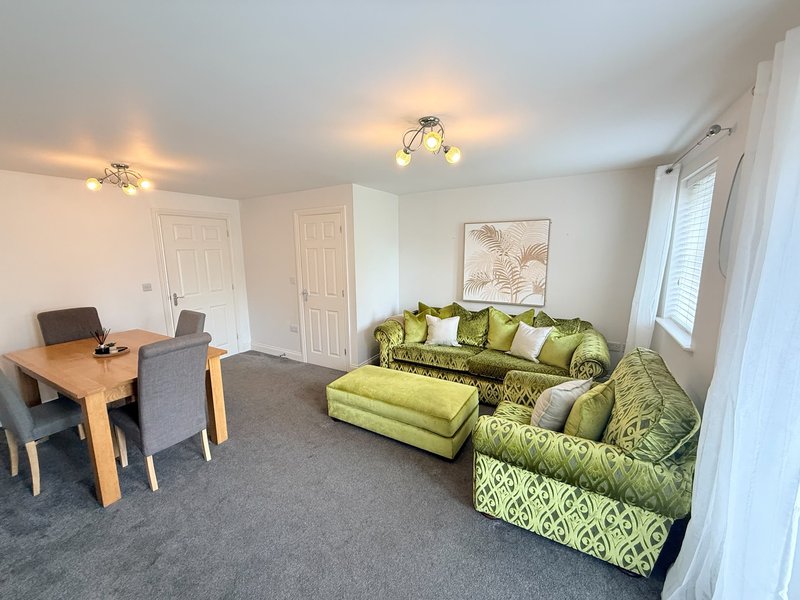 Modern living room with green patterned sofa, wooden desk, chairs and wall art