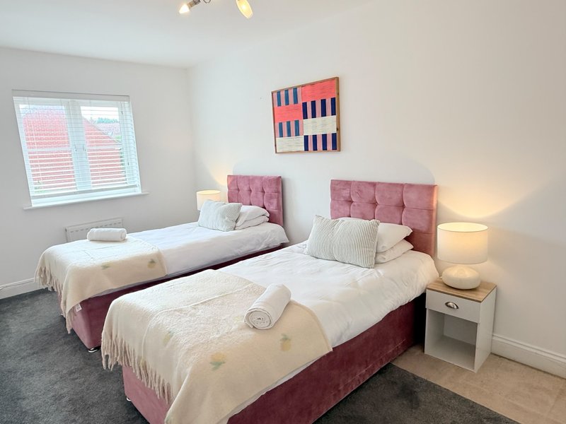 Bright twin bedroom with pink upholstered headboards, white bedding, side tables and wall art