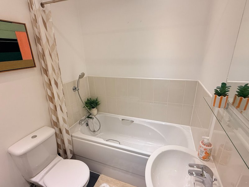 Small bathroom with white toilet, bathtub, shower curtain, and potted plants on shelf