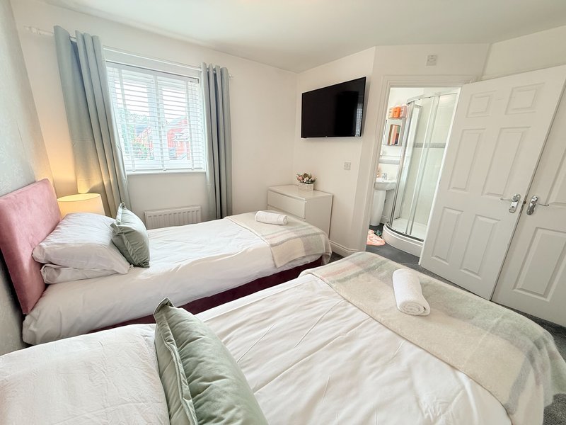 Bright bedroom with two single beds, pink headboard, wall-mounted TV, window with curtains