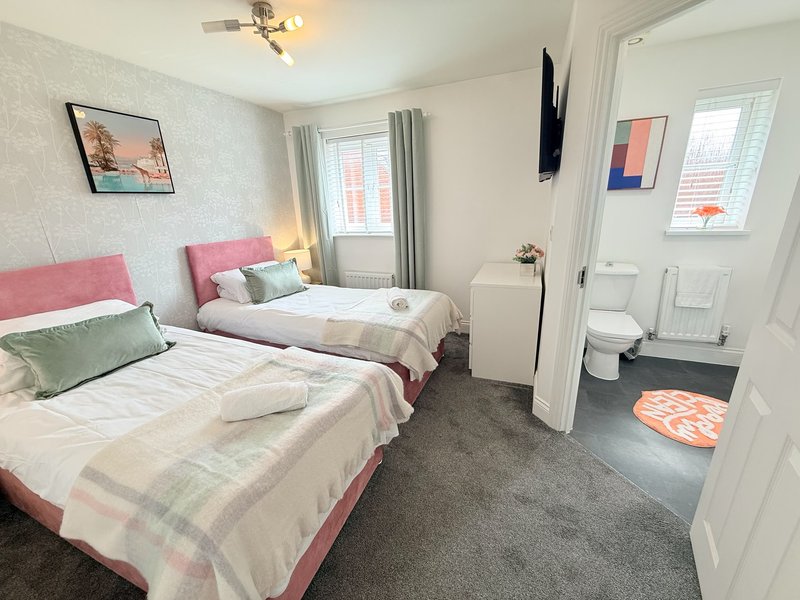 Bright bedroom with two single beds, pink headboards, and en-suite bathroom visible