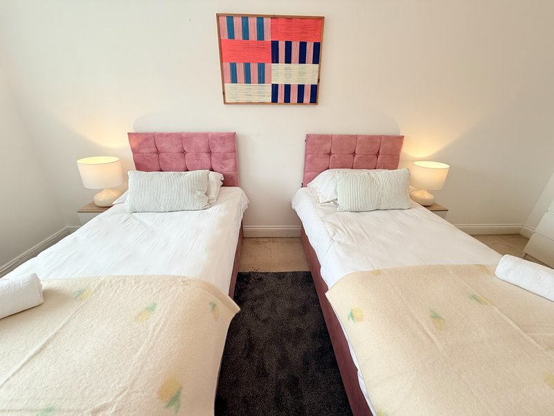 Twin bedroom with pink headboards, white bedding, bedside lamps and abstract wall art