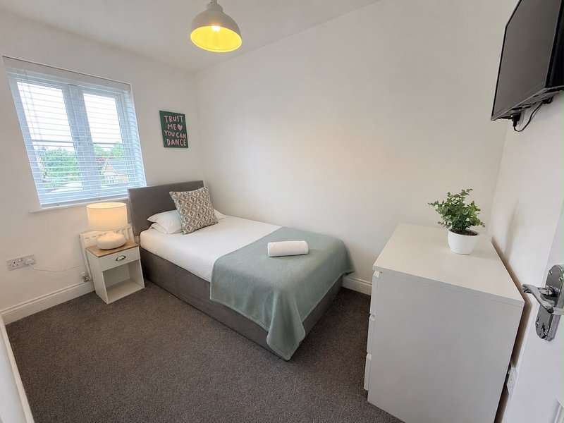 Compact bedroom with single bed, bedside lamp, small desk, wall-mounted TV and window.