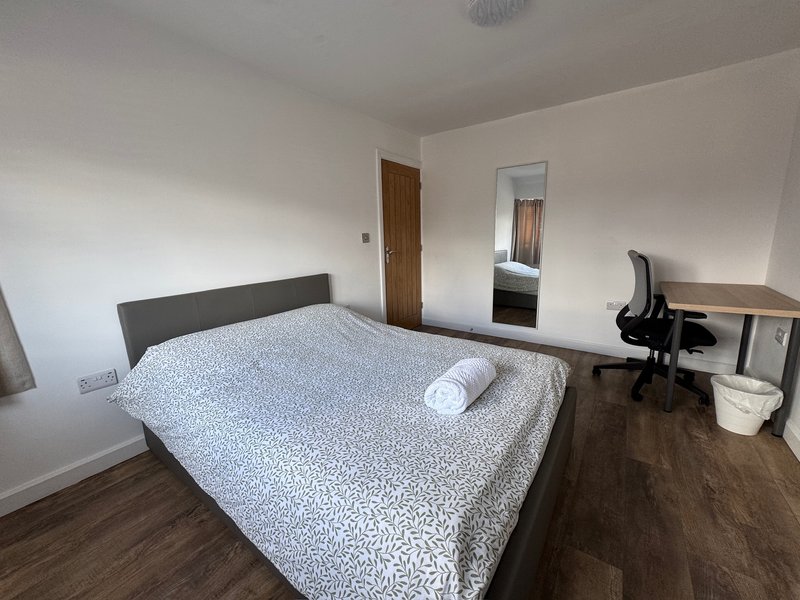 Bedroom with double bed, wooden flooring, desk with chair and mirror