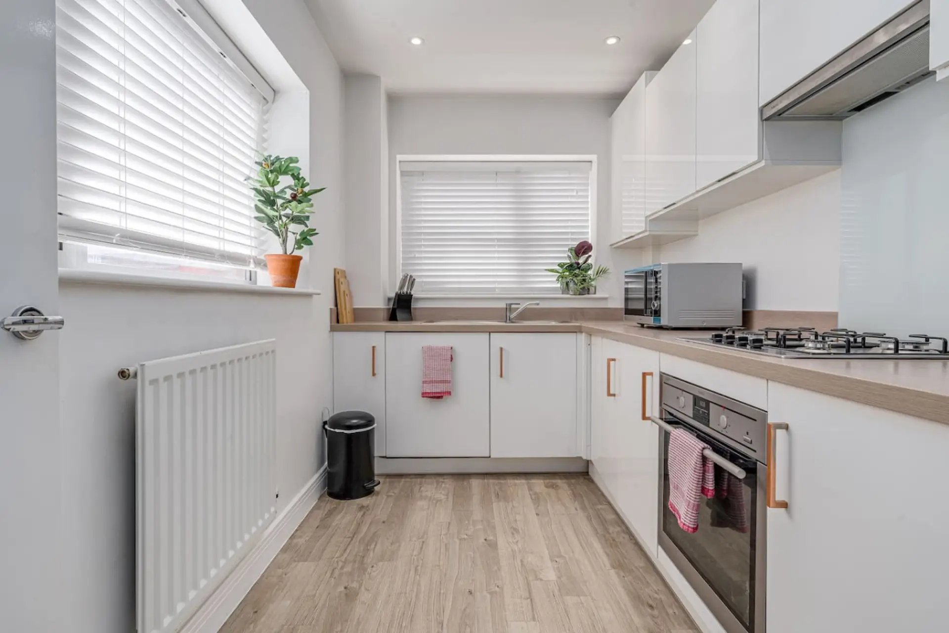 Modern white kitchen with wooden countertops, gas hob, oven and potted plants on windowsill