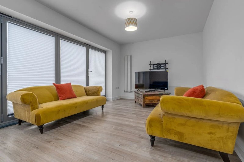 Modern living room with two yellow sofas, red cushions, wooden flooring and TV unit