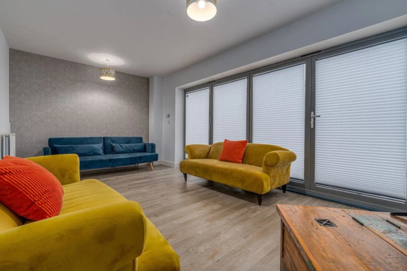 Modern living room with yellow and blue upholstered sofas, wooden table, and large sliding glass doors