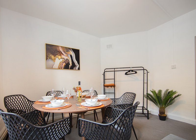 Modern dining area with round wooden table, four upholstered chairs, potted plant, and wall art