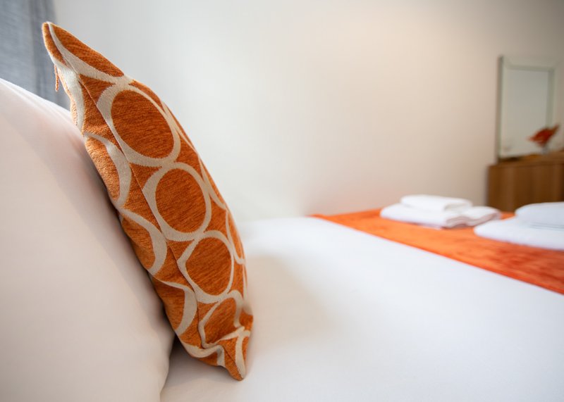 Bedroom with white bed, orange geometric patterned cushion and white pillows