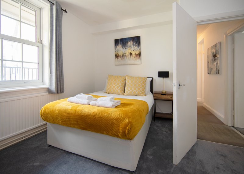 Modern bedroom with yellow bed, large window, artwork on wall and adjacent bathroom