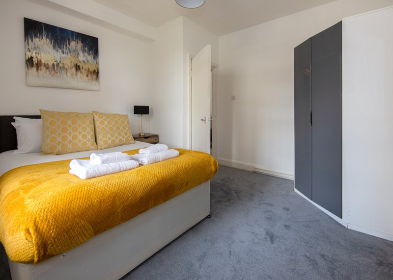 Modern bedroom with yellow bed, white towels, cushions, wall art and grey flooring