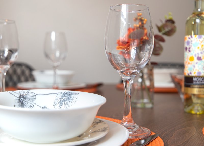 Dining table set with white bowls, wine glasses, and orange table runner
