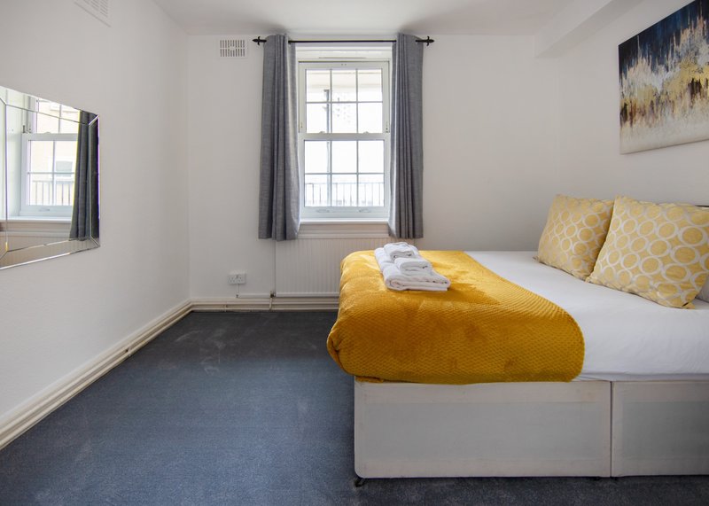 Bright bedroom with double bed, yellow bedding, patterned cushions, and large window