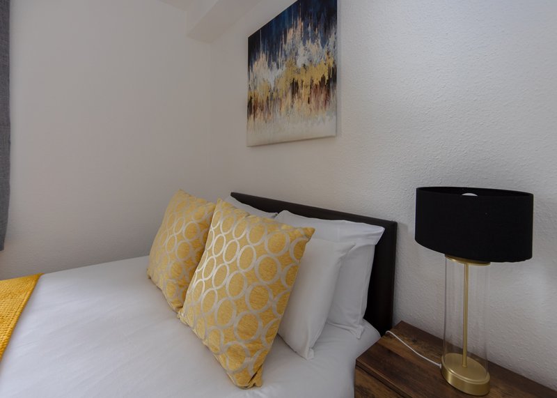 Bedroom with double bed, yellow patterned cushions, white bedding, and modern table lamp