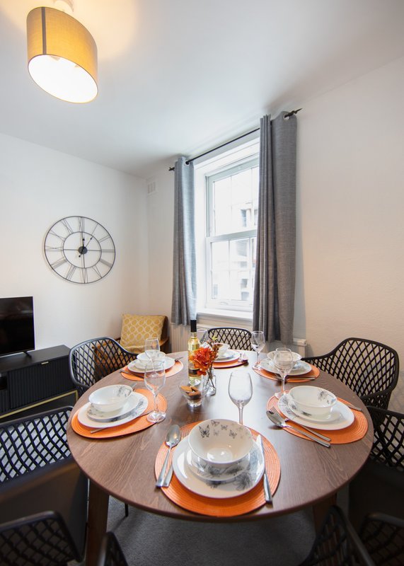 Dining room with round wooden table set for four, patterned chairs, window with grey curtains, and ceiling lamp