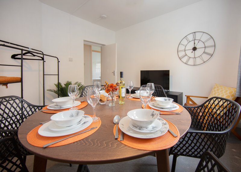 Dining room with round wooden table, place settings, black chairs, and wall clock
