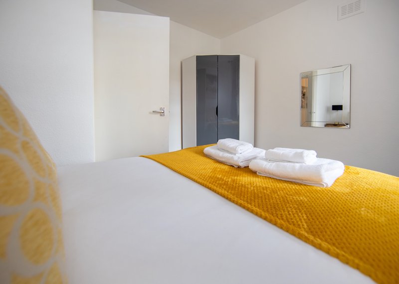 Bright modern bedroom with double bed, yellow throw, white pillows and wardrobe