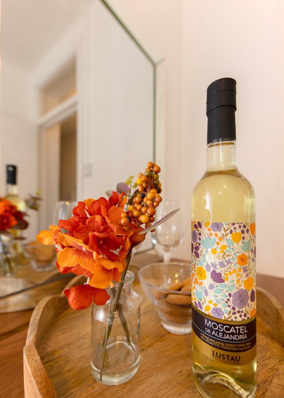 Wooden table with wine bottle, orange flowers in glass vase, and modern interior background
