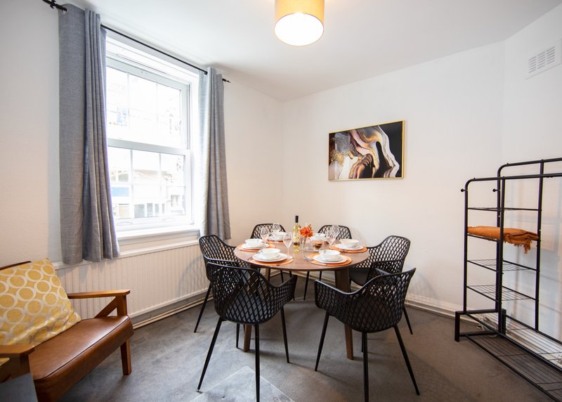 Bright dining room with round table, black chairs, window with grey curtains, and wall art