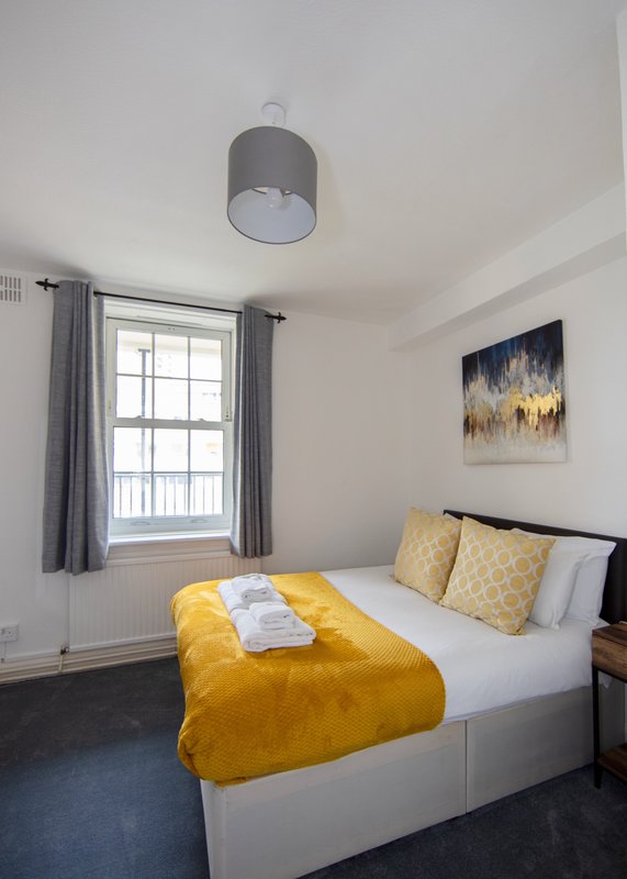 Bedroom with double bed, yellow bedding, grey pendant light, window with curtains