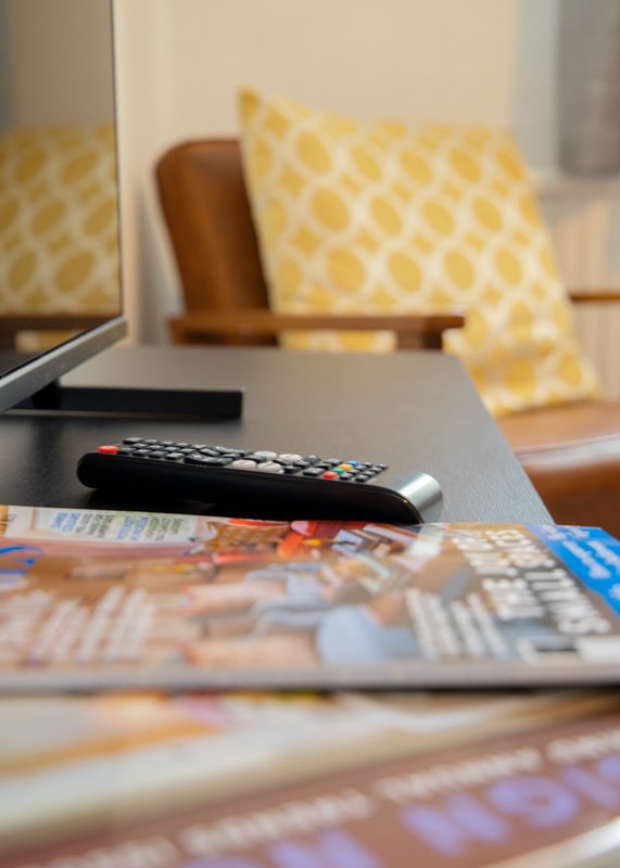 Living room detail with remote control, magazines, yellow patterned cushions and brown chair