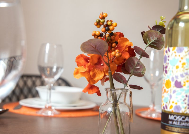 Dining table with orange flower arrangement, wine glasses, place settings and bottle