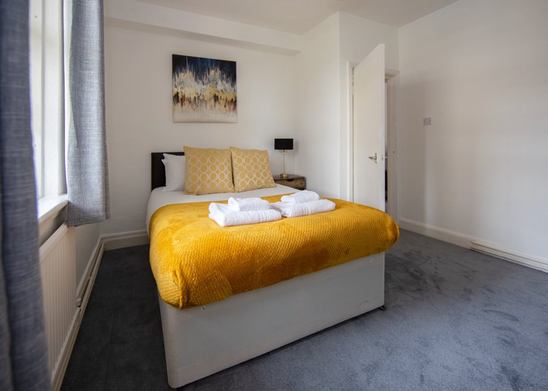 Modern bedroom with double bed, yellow bedspread, cushions, and white towels