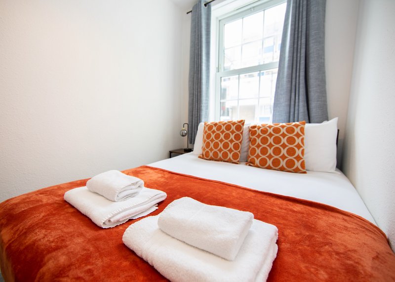 Bright bedroom with double bed, orange bedding, white pillows and folded towels