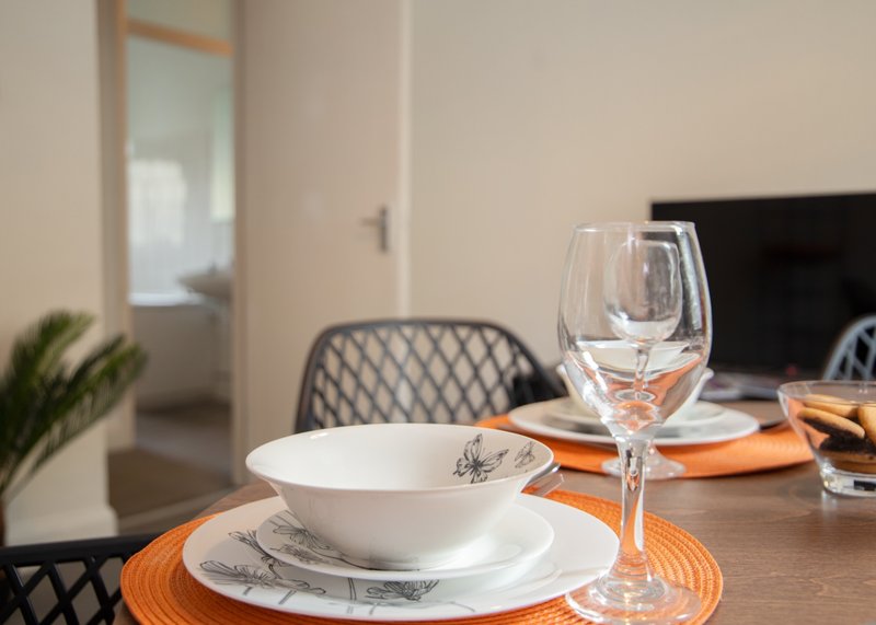 Dining table set with white plates, glasses, and orange placemat in modern interior