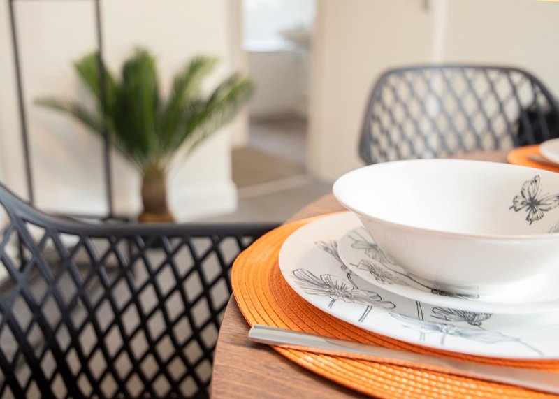 Dining table setting with place settings, plant, and patterned chairs in background