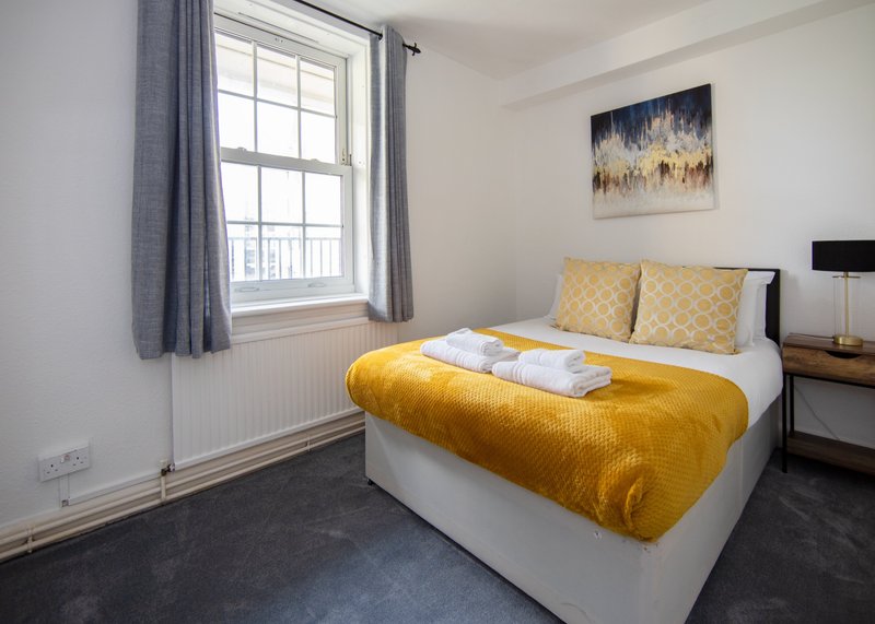 Bright bedroom with double bed, yellow bedding, window with grey curtains, and wall art