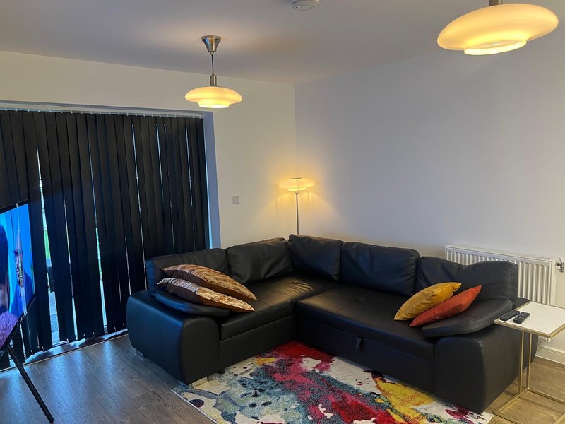 Modern living room with black corner sofa, colorful cushions, pendant lights and dark curtains