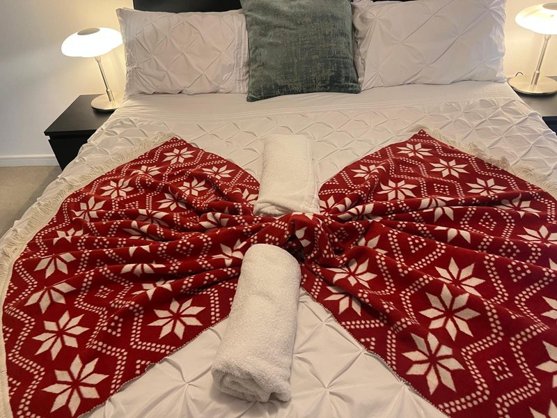 Bedroom with double bed, red patterned throws, white pillows and bedside lamps