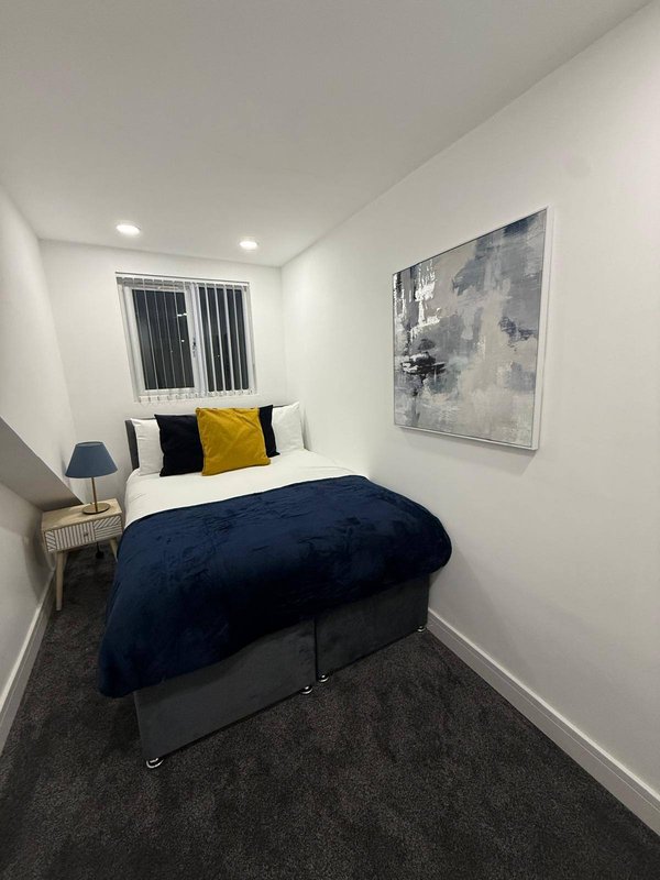 Compact bedroom with double bed, navy bedding, decorative pillows, wall art, and window with blinds
