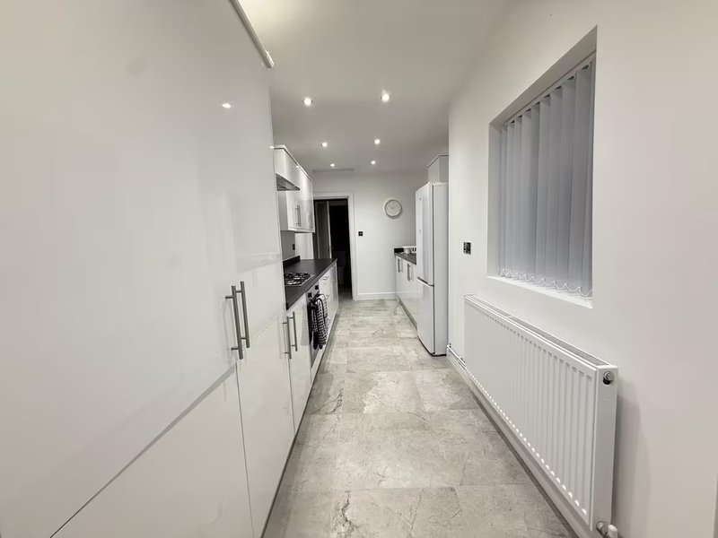 Modern narrow kitchen with white cabinetry, stainless steel appliances, and tile flooring