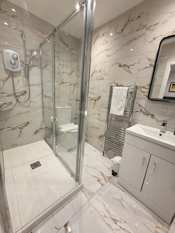 Modern bathroom with marble-effect tiles, walk-in shower enclosure, white vanity and heated towel rail