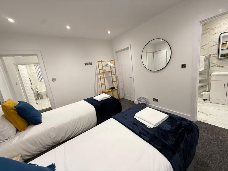 Modern bedroom with two single beds, colorful pillows, round mirror and ensuite bathroom visible