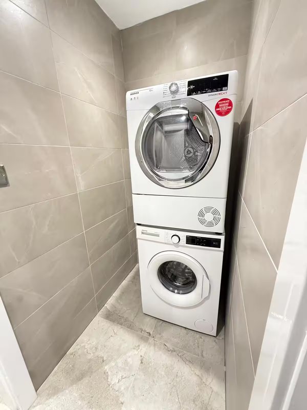 Laundry room with stacked white washing machine and tumble dryer, tiled walls