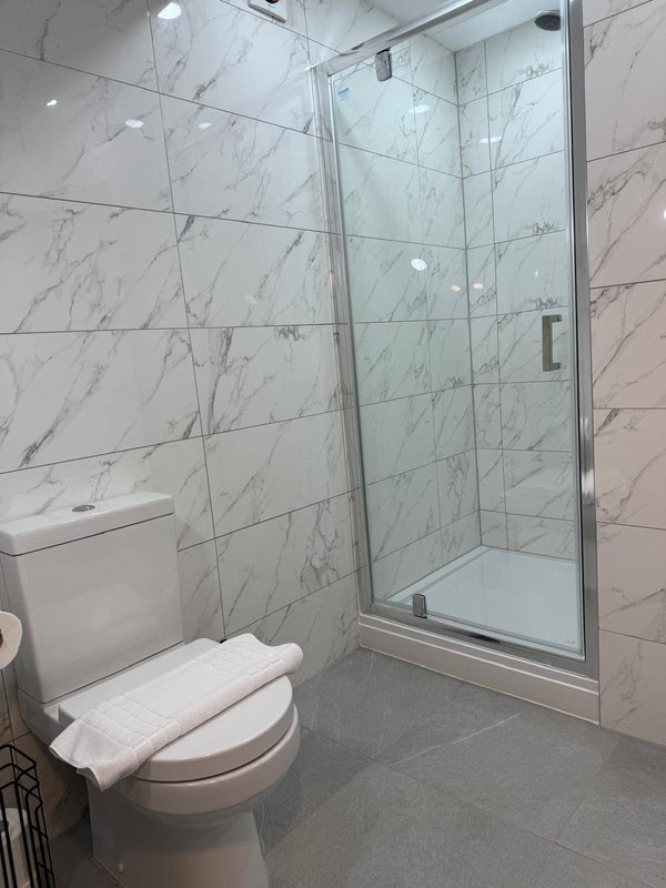 Modern bathroom with marble-effect tiled walls, glass shower enclosure and white toilet