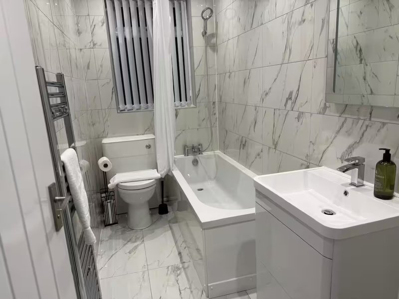 Modern bathroom with marble-effect tiles, white vanity, toilet, bathtub and shower enclosure