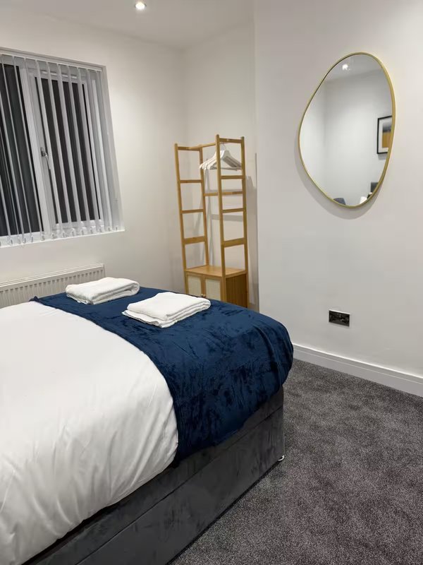 Bedroom with white bed, navy throw, wooden room divider and circular mirror