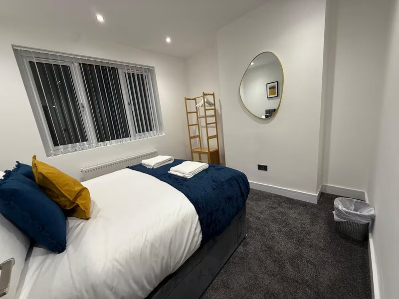 Modern bedroom with double bed, navy and yellow pillows, round mirror, and barred window