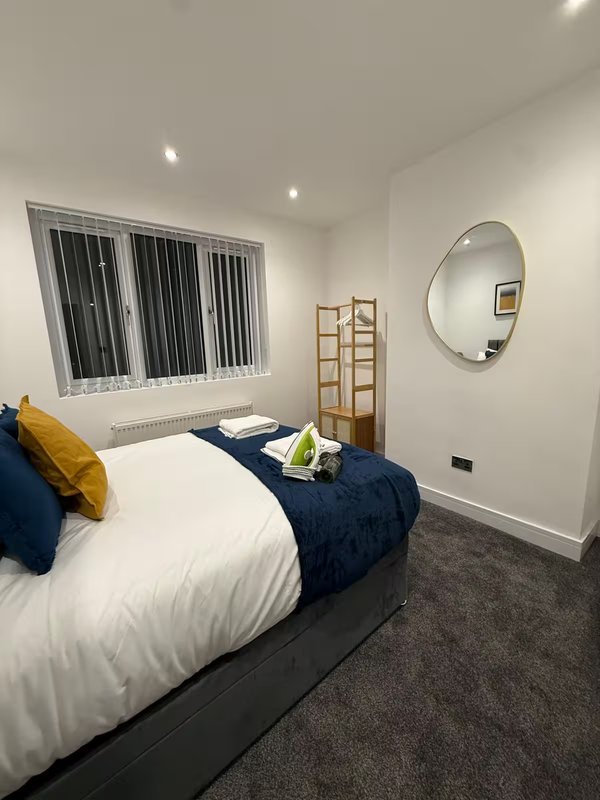 Modern bedroom with double bed, yellow pillow, round mirror and window with blinds